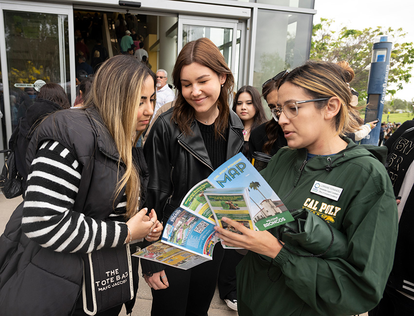 A tour guide helps two female students view a campus map.
